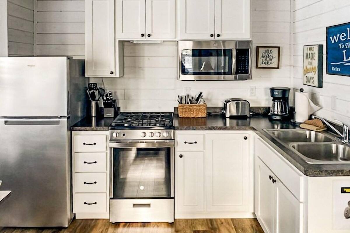 A modern kitchen with white cabinets, stainless steel appliances, and a wooden floor.