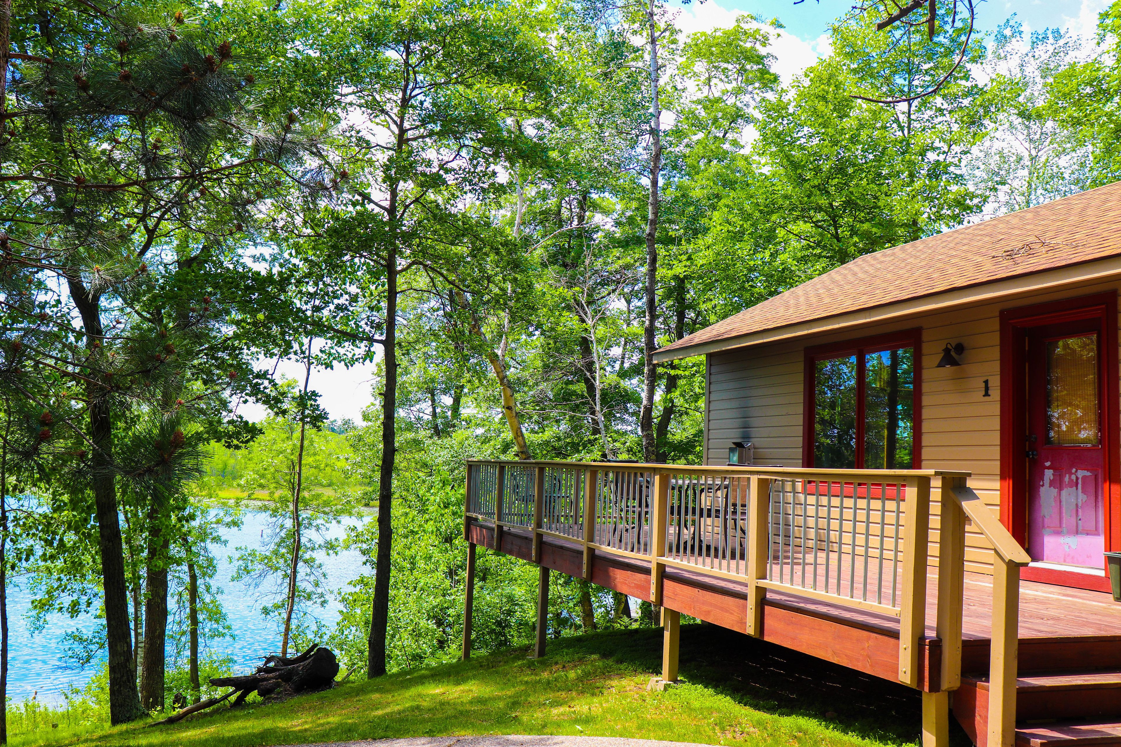 A cabin with a deck overlooking a lake, surrounded by trees.