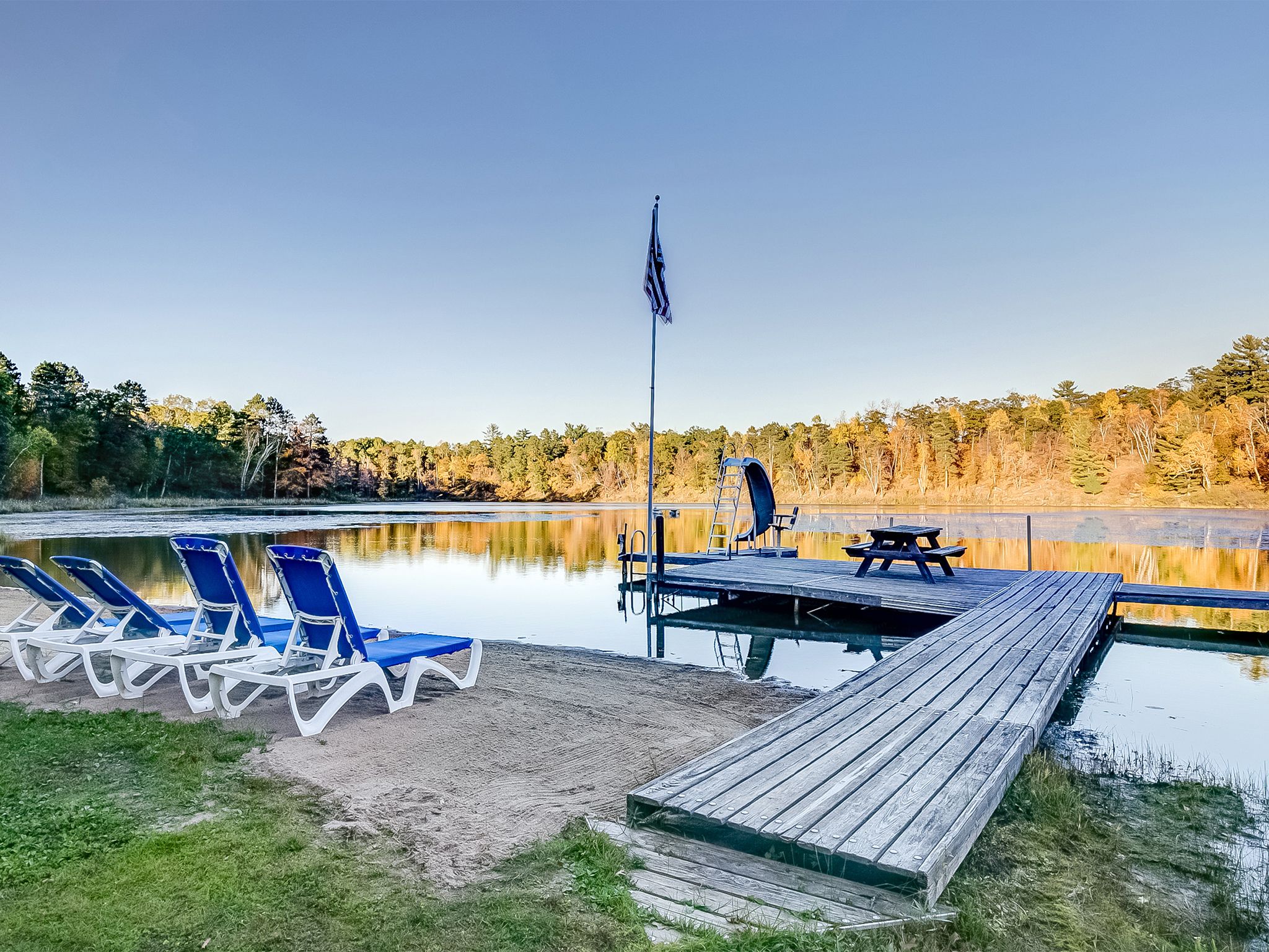 A lakeside dock with lounge chairs, a picnic table, and a flagpole.