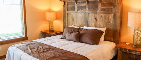 A bedroom with a large bed, wooden headboard, two bedside tables with lamps, and a window with blinds.