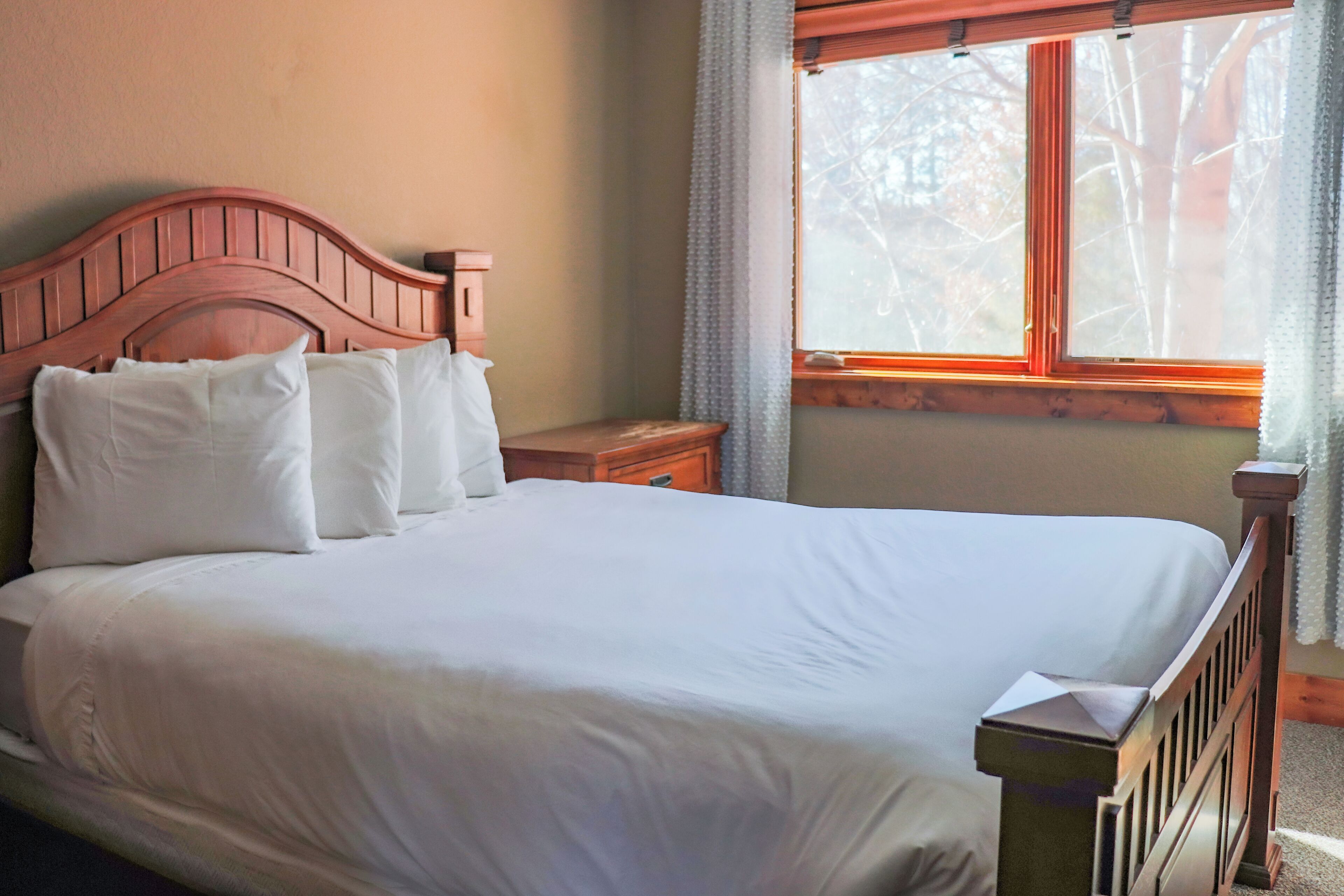 Una cama bien hecha con sábanas blancas y un cabecero de madera en una habitación con ventana.