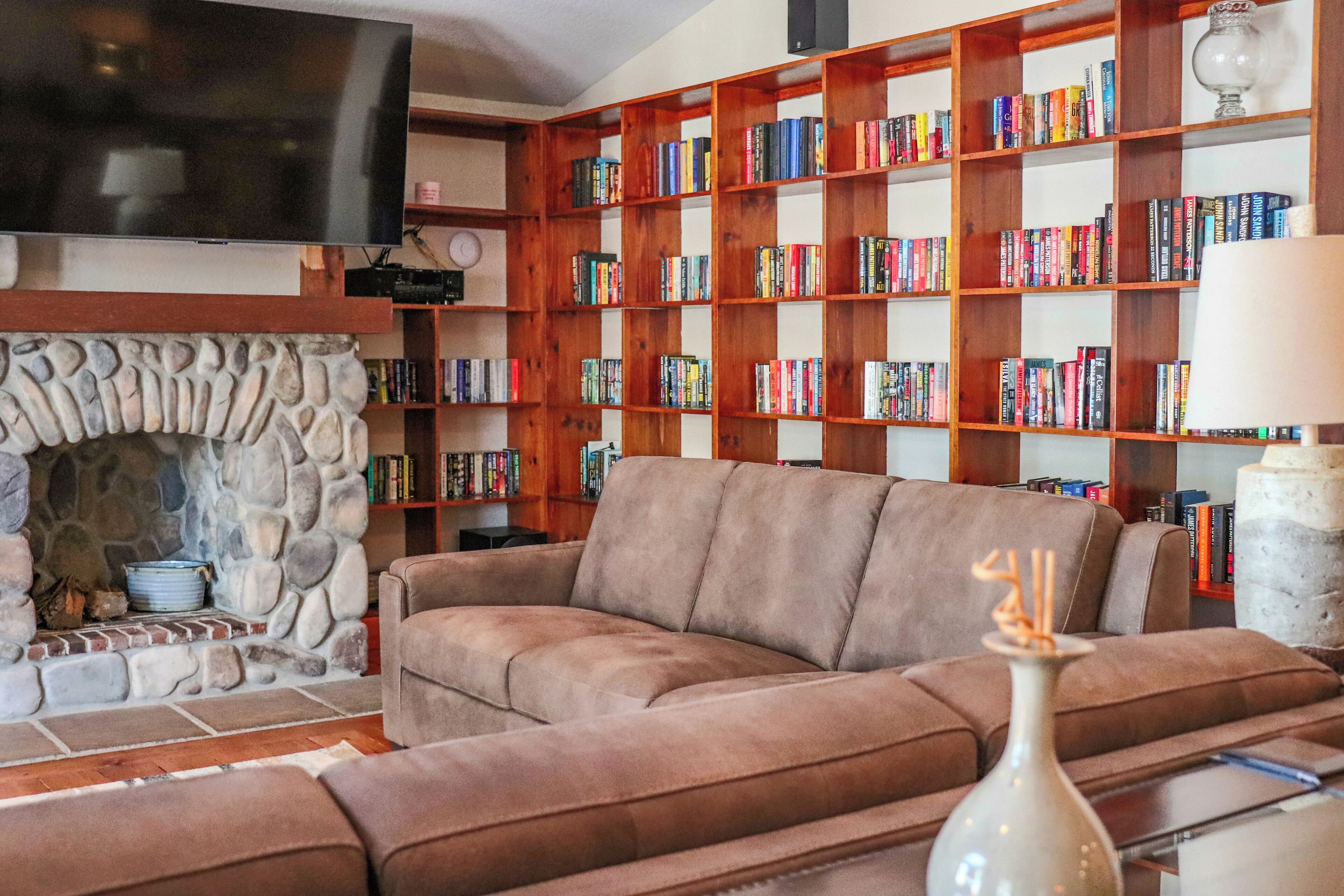 Ein Wohnzimmer mit Kamin aus Stein, einer großen Bücherwand, einem Flachbildfernseher und einem braunen Ledersofa.