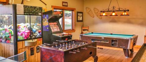 A room with a foosball table, a pool table, and a claw machine.