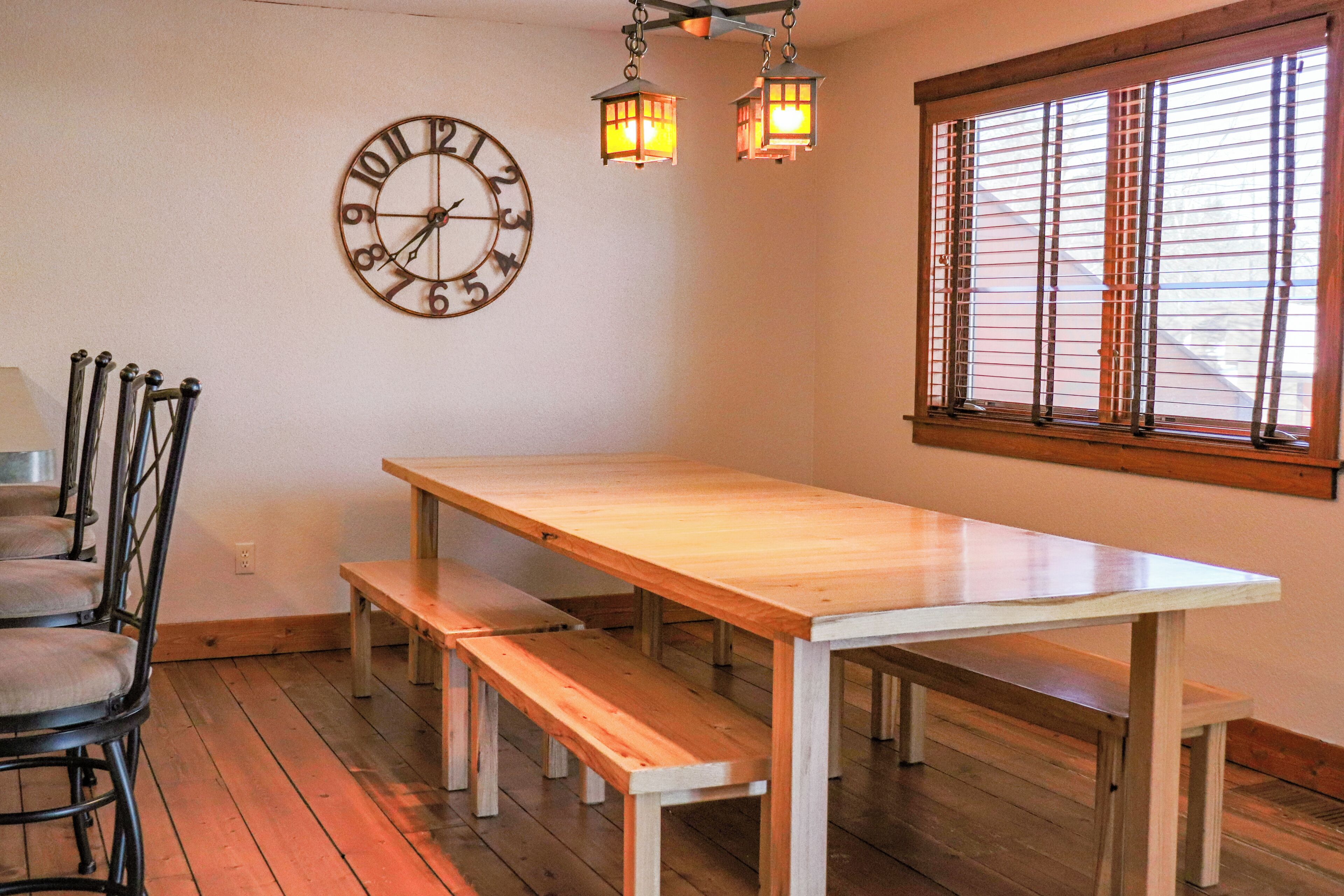 Un comedor con mesa de madera, bancos y un reloj de pared.