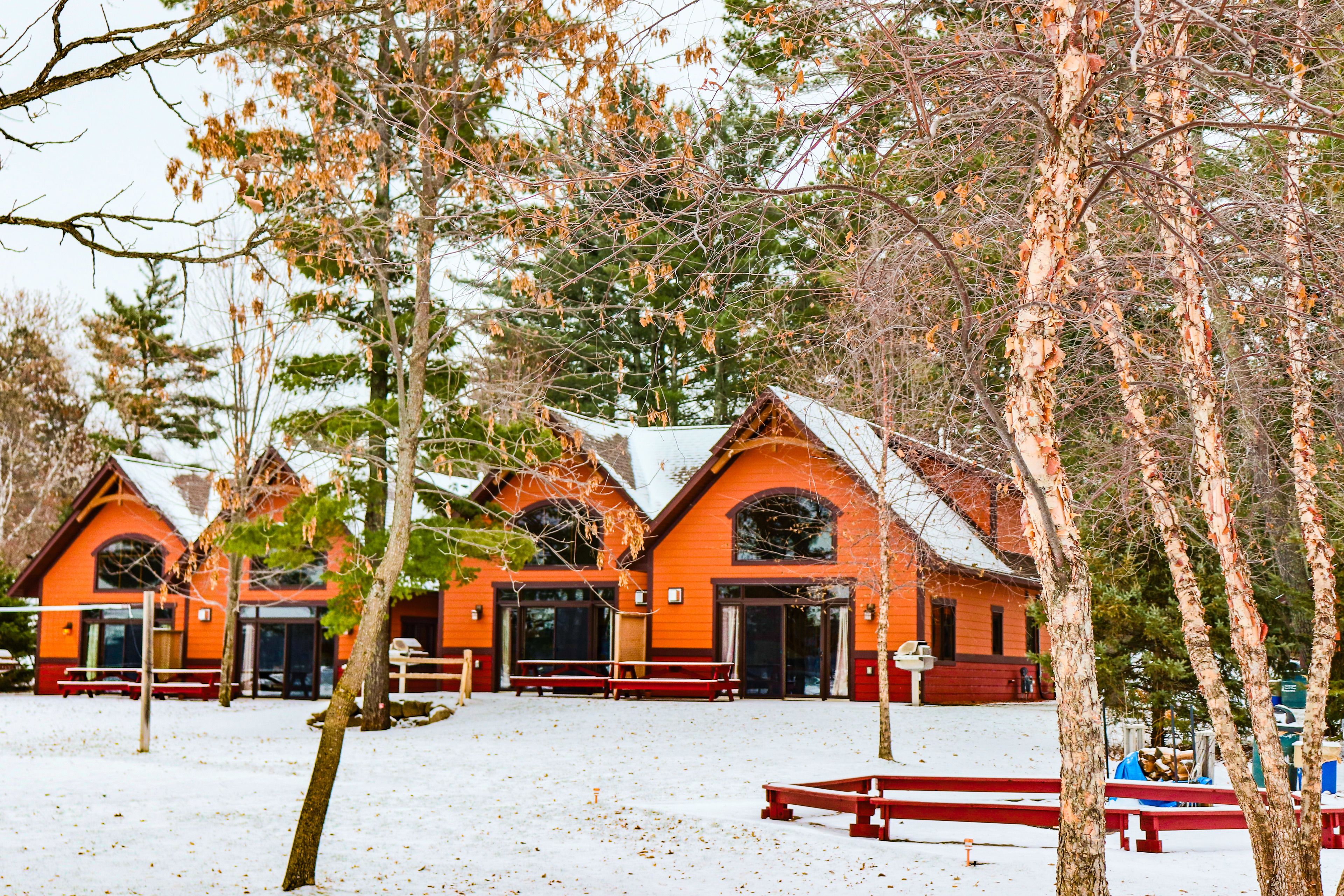 A row of wooden cabins with red roofs and large windows, surrounded by snow and trees.