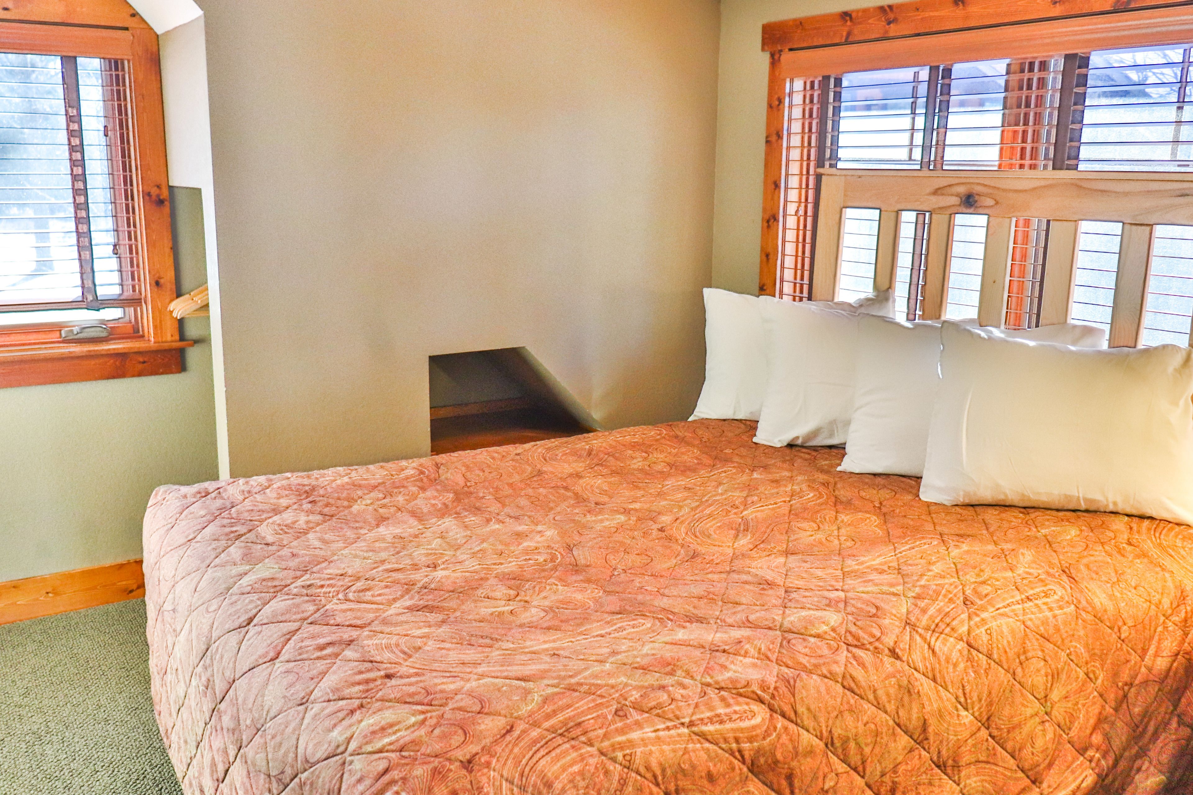A bedroom with a large bed, a wooden headboard, and a window with blinds.