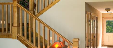 A wooden staircase with a glass railing, a leather sofa with a patterned pillow, a small wooden table with a lamp, and a patterned rug on a wooden floor.