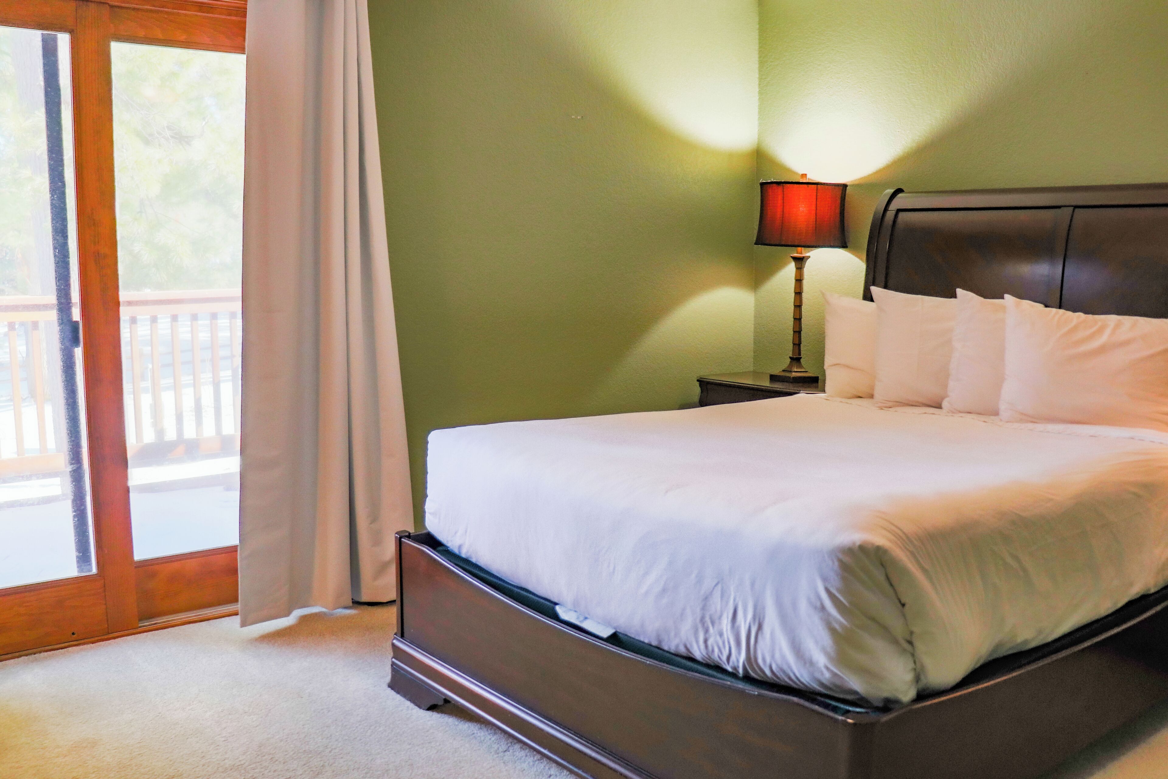 A bedroom with a bed, a nightstand, a lamp, and a view of the outdoors through a sliding door.