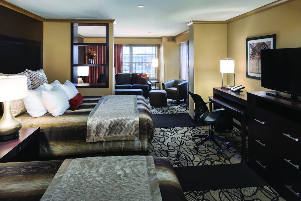 A hotel room with two beds, a desk with a computer, a TV, and a window with curtains.