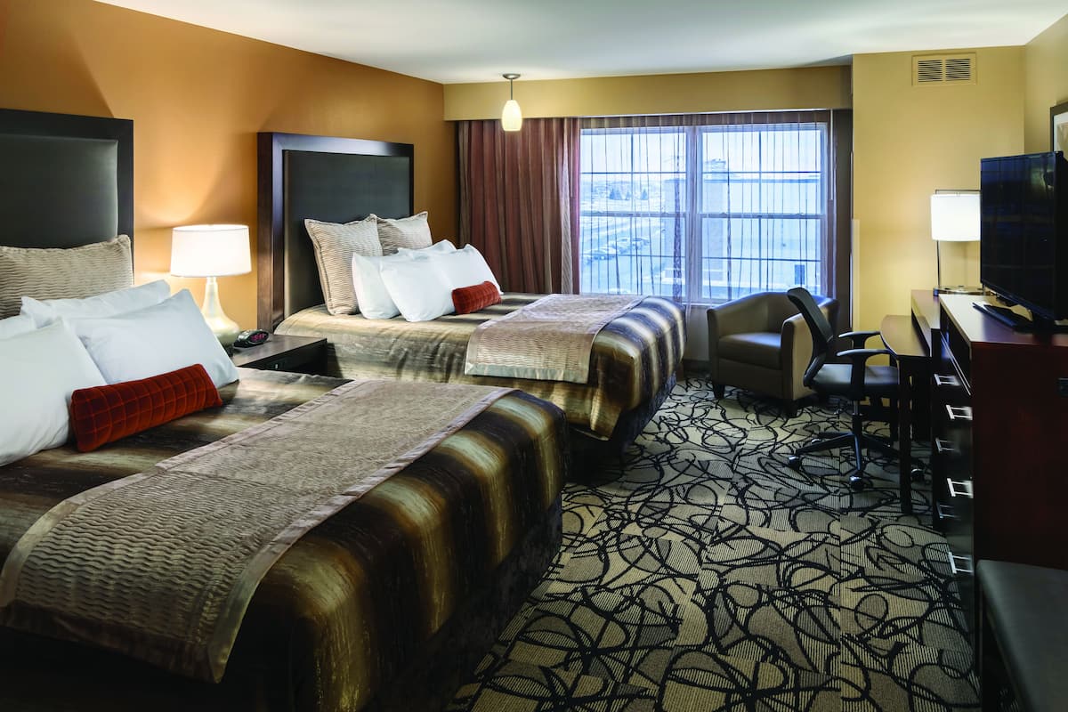 A hotel room with two beds, a desk, a chair, and a television.