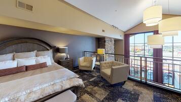 Ein Hotelzimmer mit einem großen Bett, zwei Sesseln, einem kleinen Tisch und einem Balkon mit Blick.