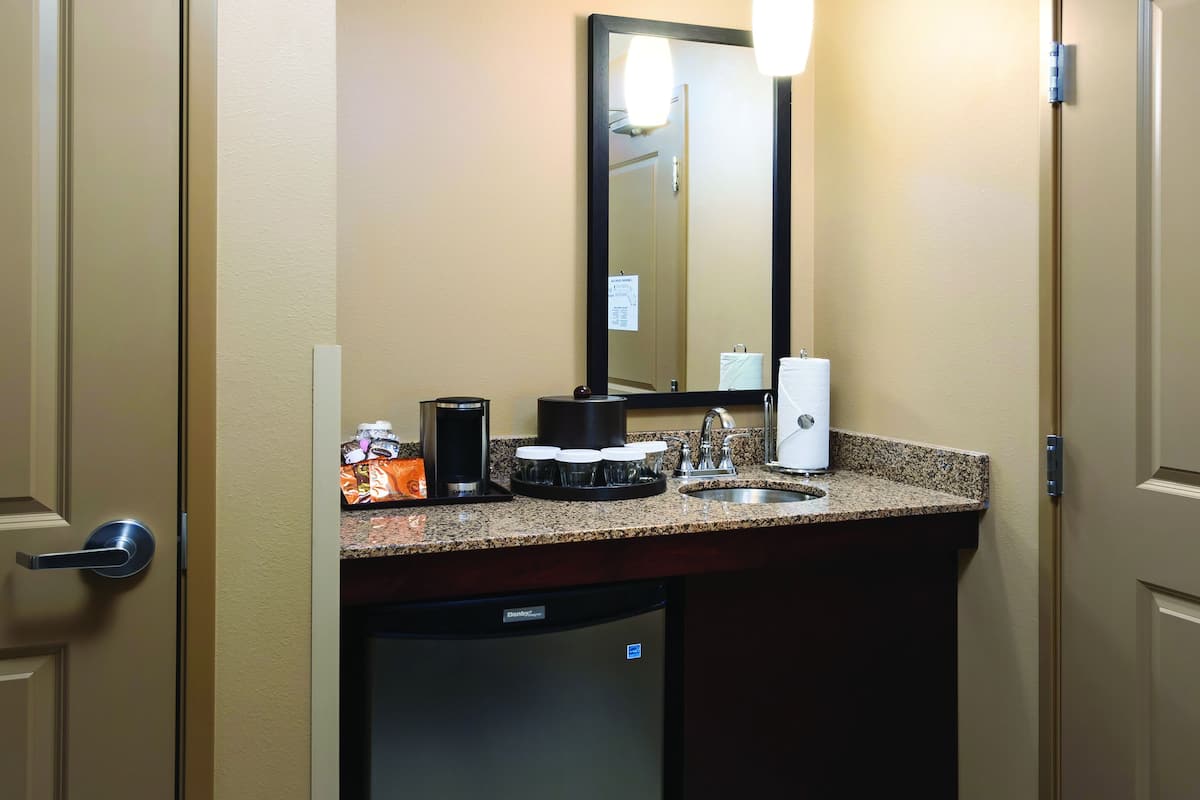 A compact hotel bathroom with a sink, mirror, and a coffee maker.