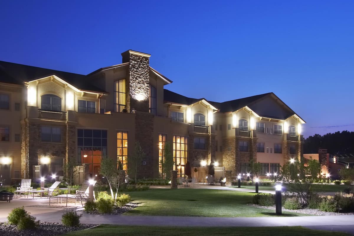 A large, multi-story hotel with a stone facade, multiple balconies, and a well-lit outdoor area with seating.
