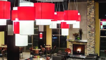 A hotel lobby with multiple tables and chairs, a fireplace, and hanging red and white pendant lights.