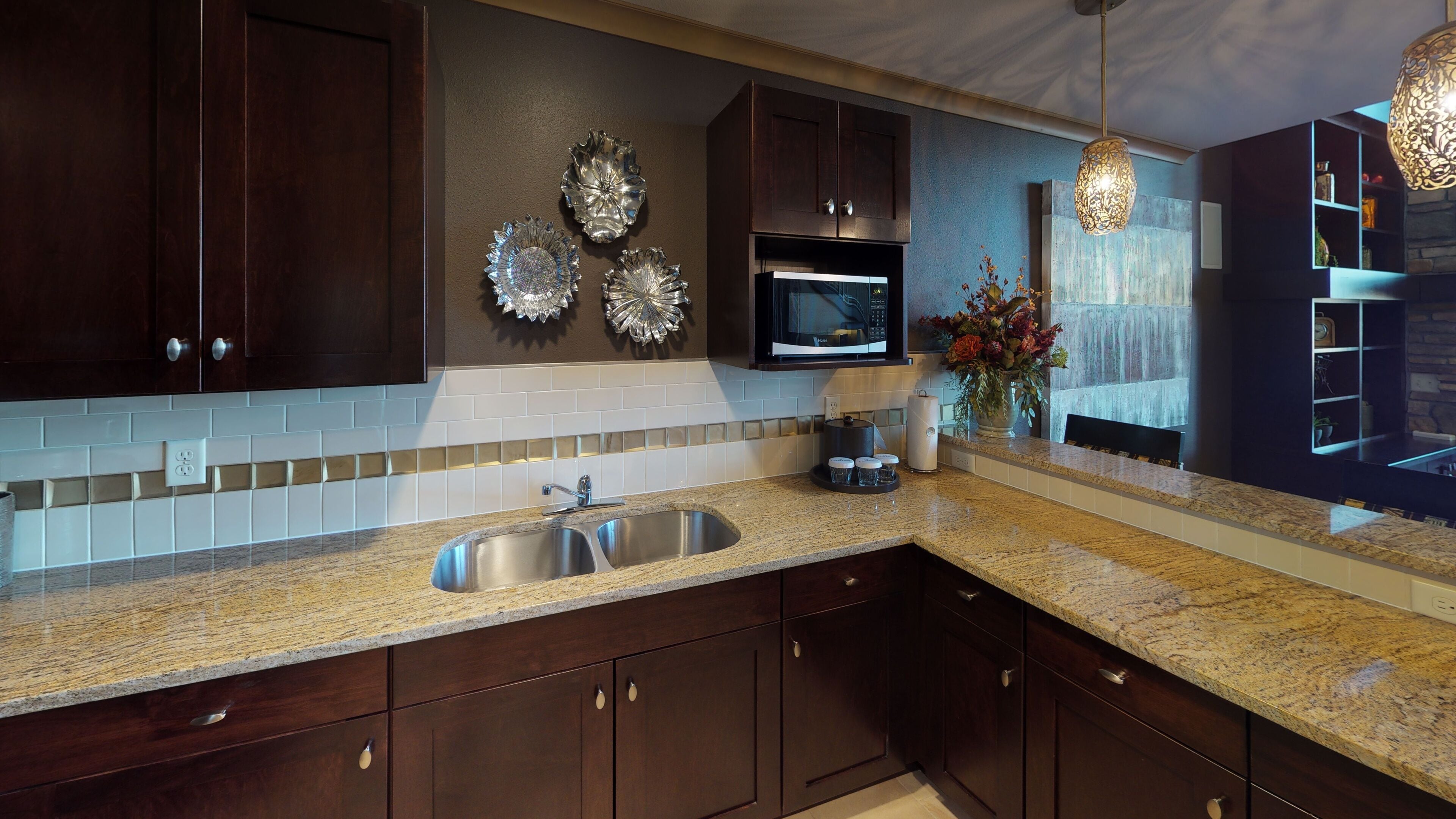 A modern kitchen with dark wooden cabinets, a granite countertop, a stainless steel sink, a microwave, and decorative wall plates.