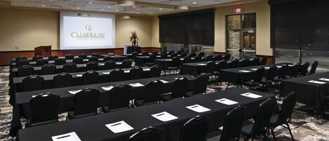 A conference room with multiple tables and chairs, a podium, and a presentation screen displaying 'ClubHouse Hotel & Suites'.