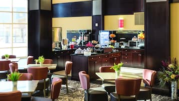 Relax in our stylish lobby, featuring a central coffee station and comfortable seating areas with potted plants.