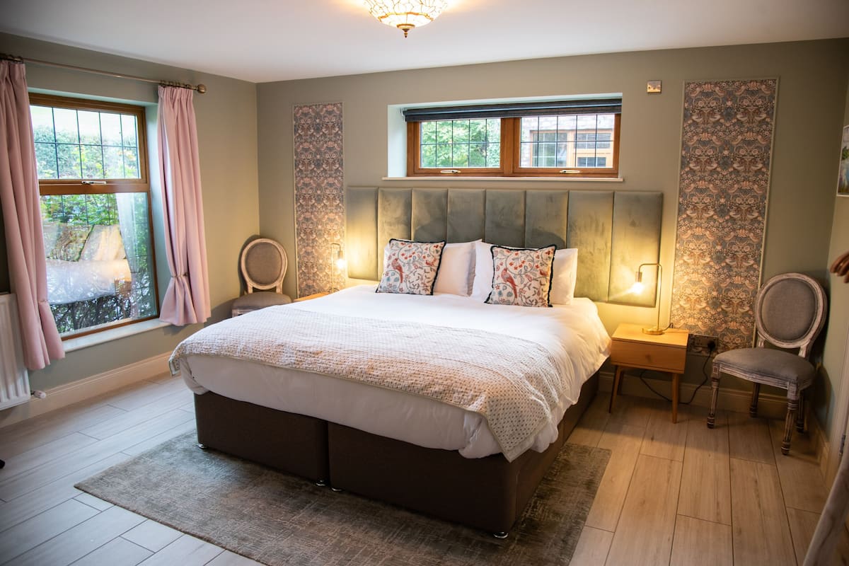 Quarto com uma cama grande, duas mesas de cabeceira, uma cadeira e uma janela com cortinas.