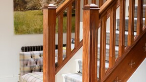 A wooden staircase with a white base and a view of a living room with a plaid sofa and a painting of a tree. - Blackwell House (Craigavon)