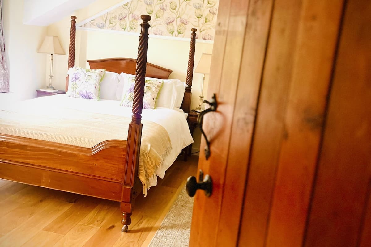 Uma cama de madeira com dossel e cortina, uma mesa de cabeceira com abajur e um guarda-roupa de madeira com um aviso.