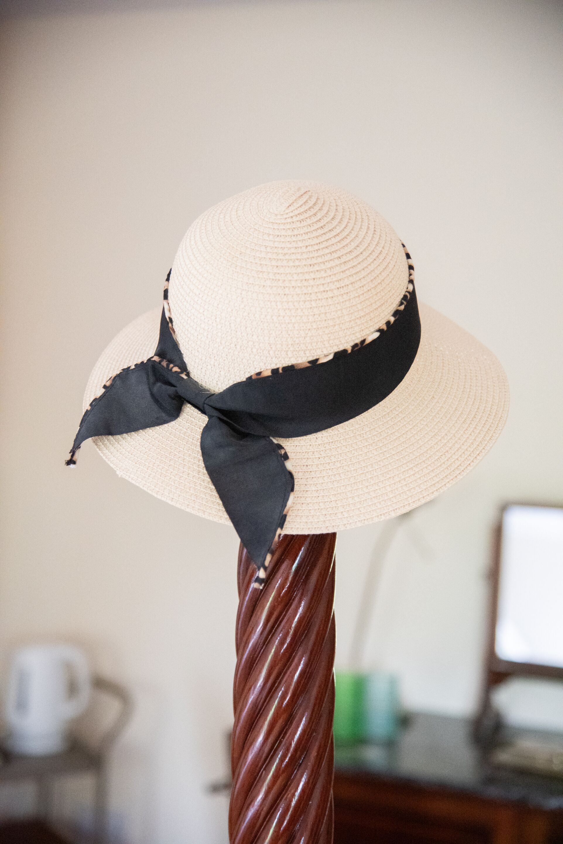 Un sombrero de paja con un lazo negro sobre un soporte de madera.