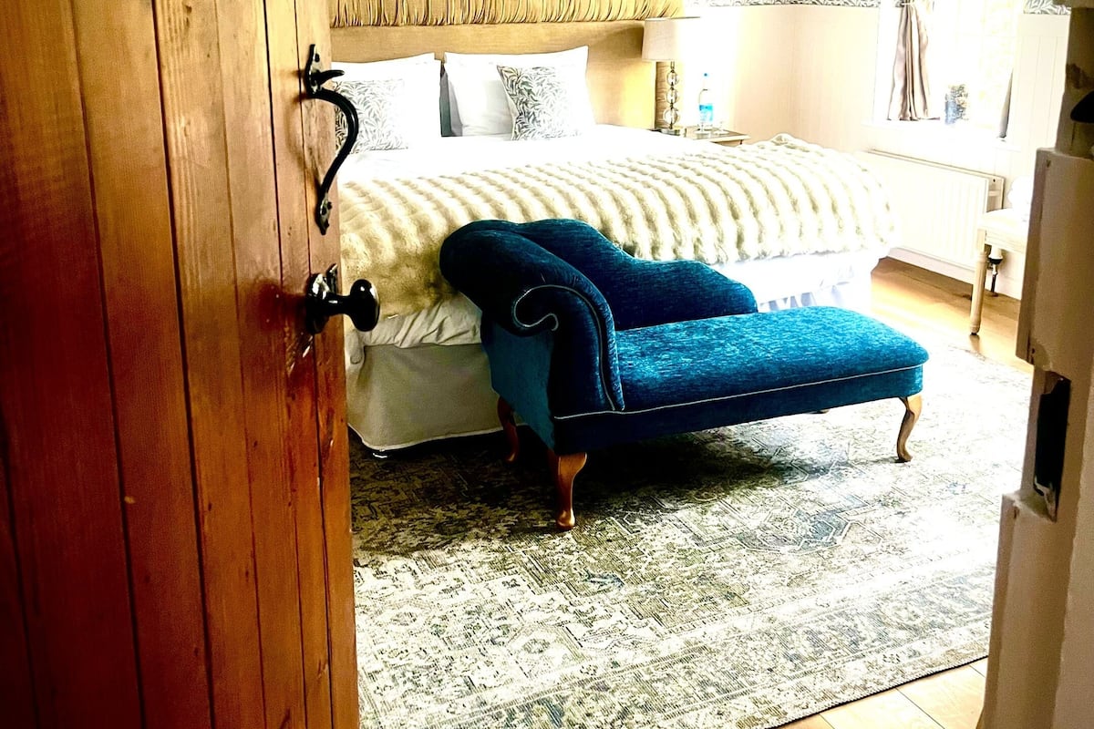 Um quarto com cama, uma cadeira azul, um tapete estampado e uma porta de madeira.