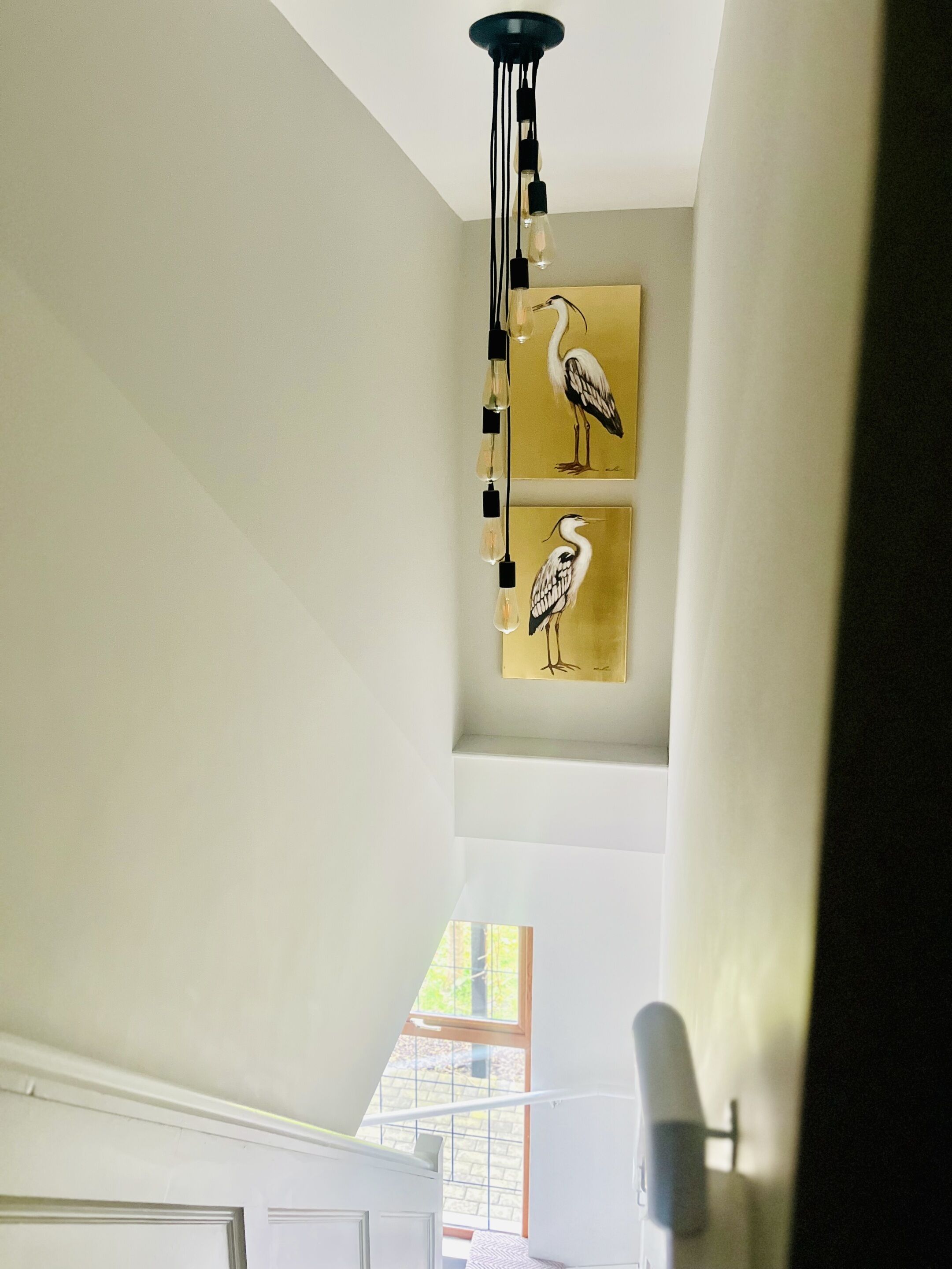 Una escalera con una lámpara moderna y dos cuadros de pájaros colgados en la pared.