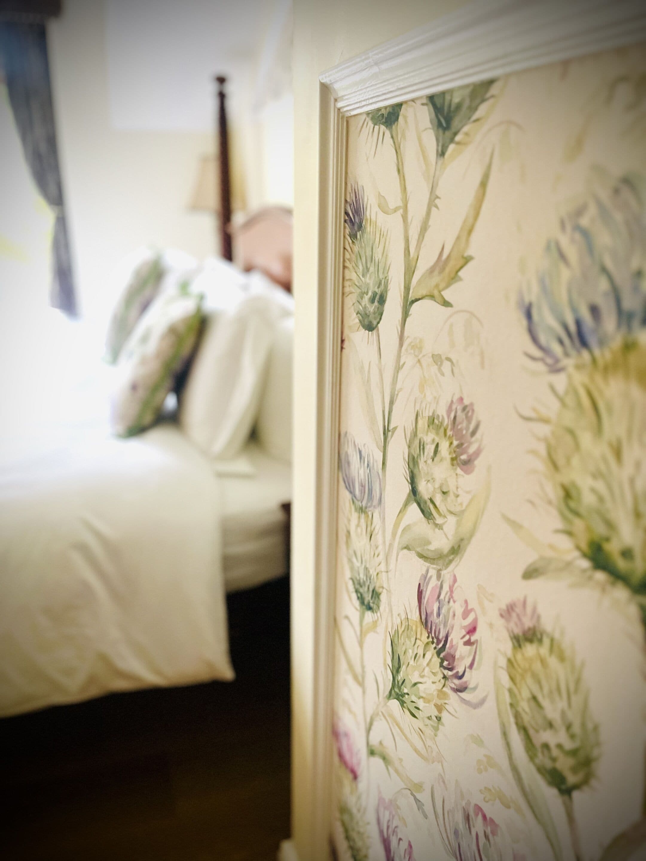 A bedroom with a bed, pillows, and a floral wallpaper.