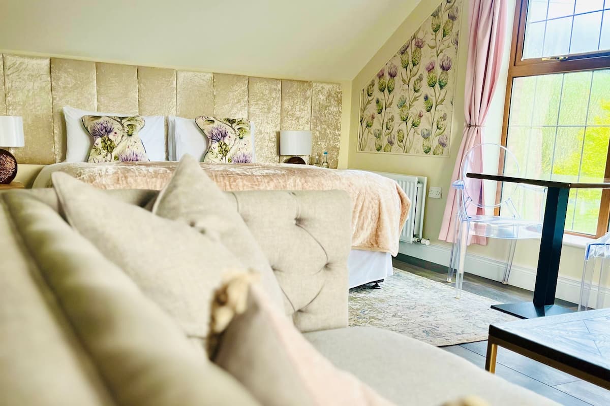 Quarto com cama, sofá, radiador, janela com cortinas e parede com papel de parede floral.