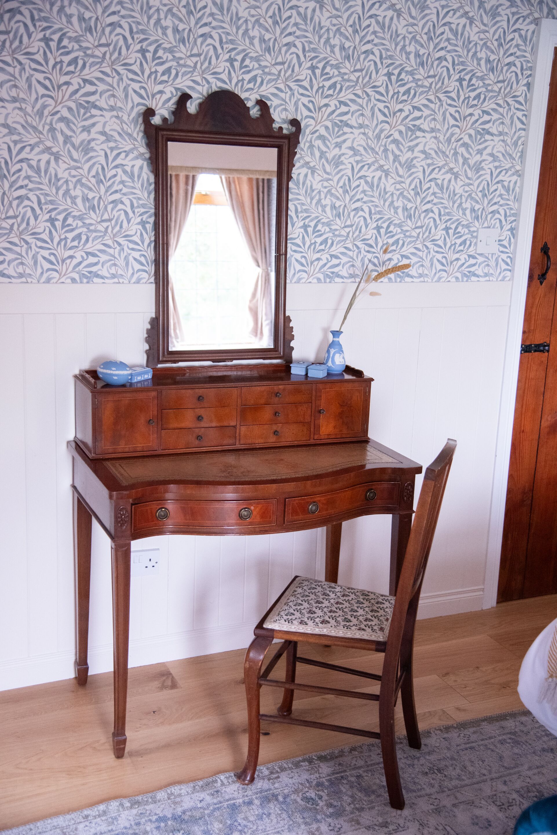 Un aparador de madera con espejo, una silla y un papel tapiz estampado.