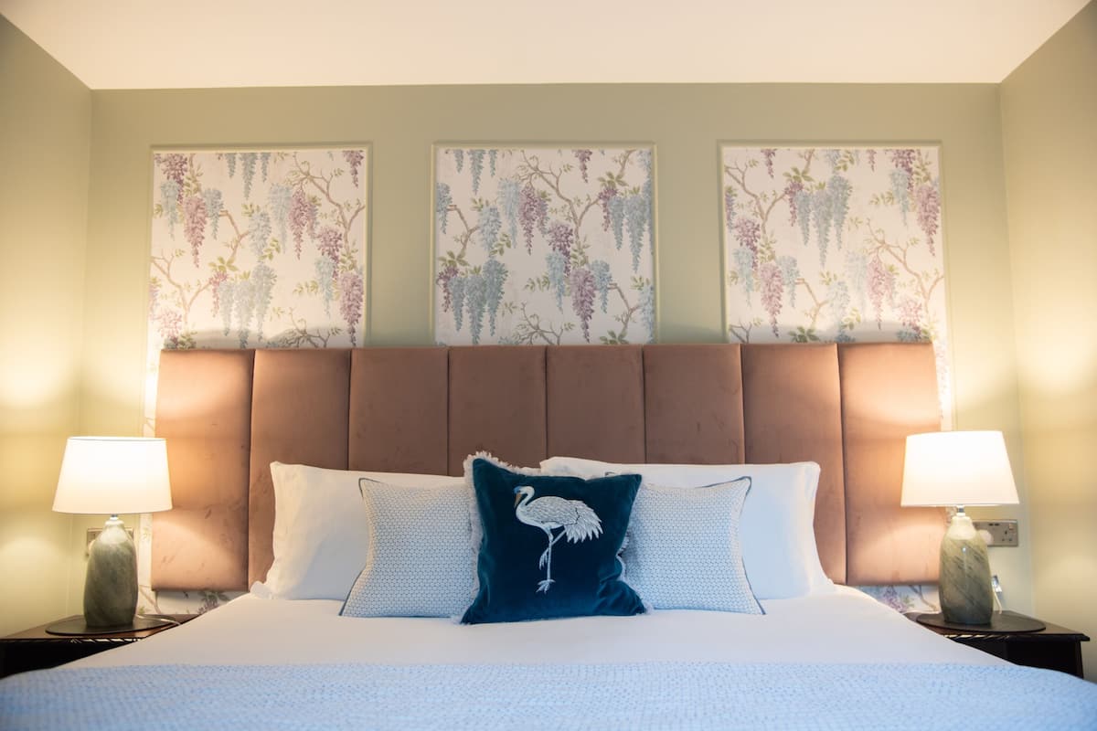 Quarto de hotel com uma cama grande, duas luminárias de cabeceira e três quadros florais sobre a cama.