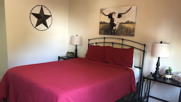 A bed with a red blanket, two bedside tables with lamps, a star decoration, and a painting of a bull. - River Rock Inn (Mariposa)