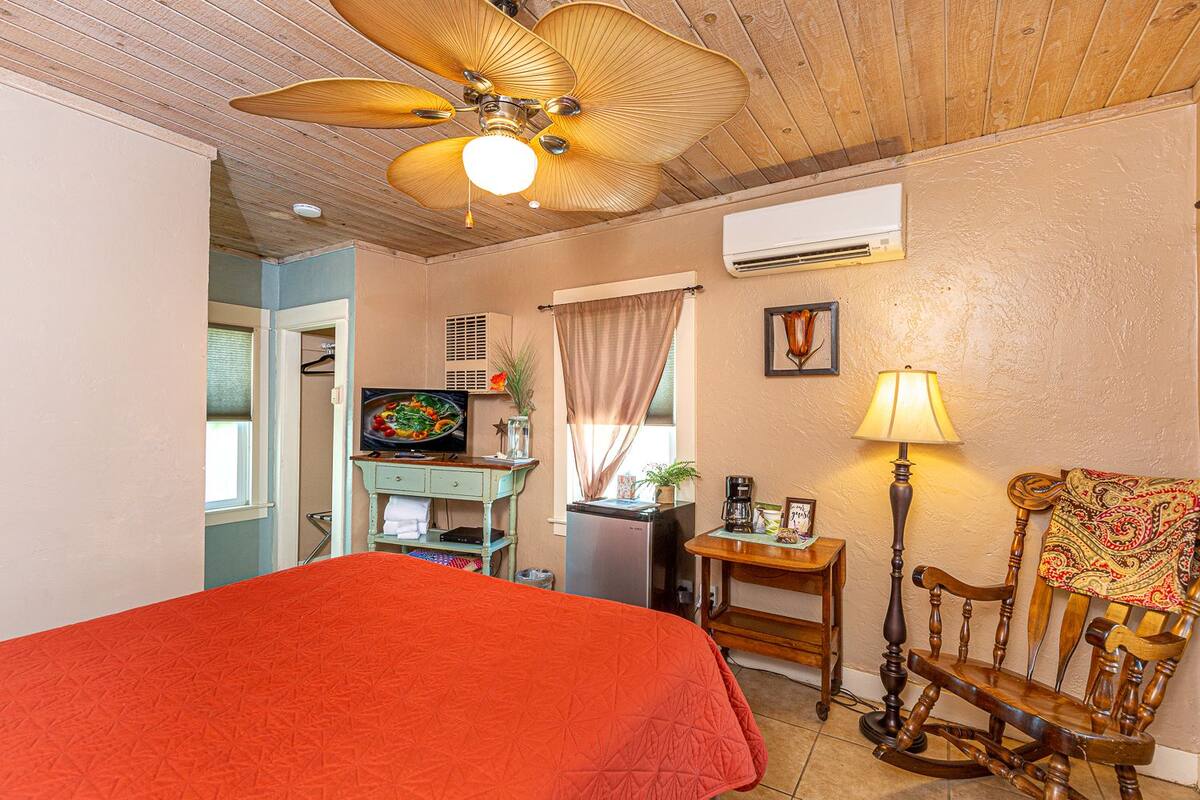 A bedroom with a bed, a desk, a chair, a ceiling fan, an air conditioner, and a window.