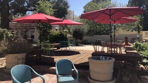An outdoor patio area with wooden tables and chairs, red umbrellas, and potted plants. - River Rock Inn (Mariposa)