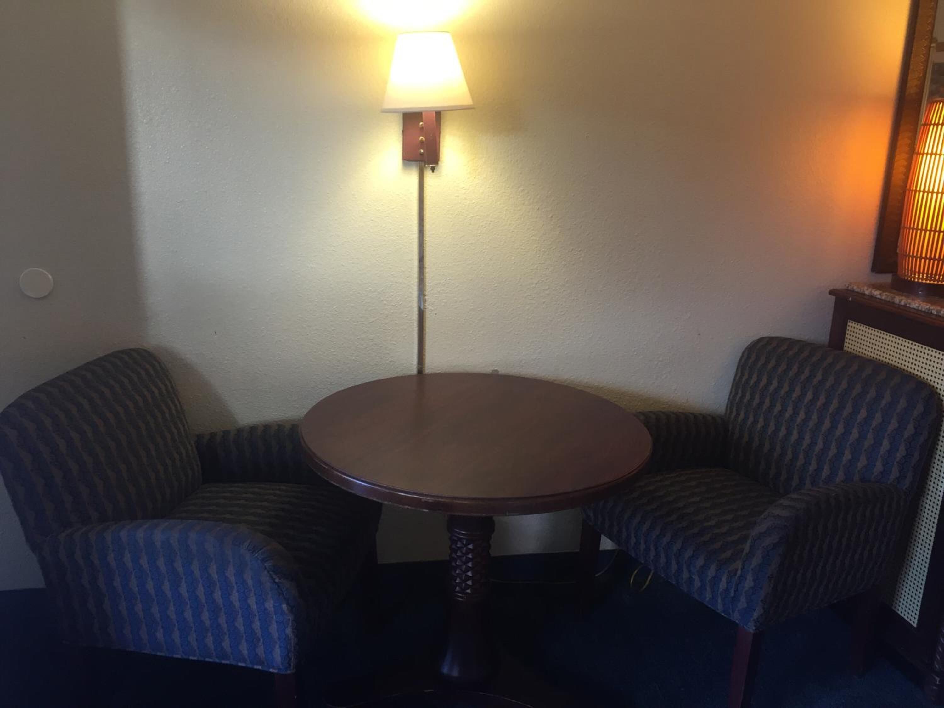 Ein kleiner runder Tisch mit zwei gepolsterten Stühlen, einer Wandlampe und einem hölzernen Beistelltisch mit einer Lampe.