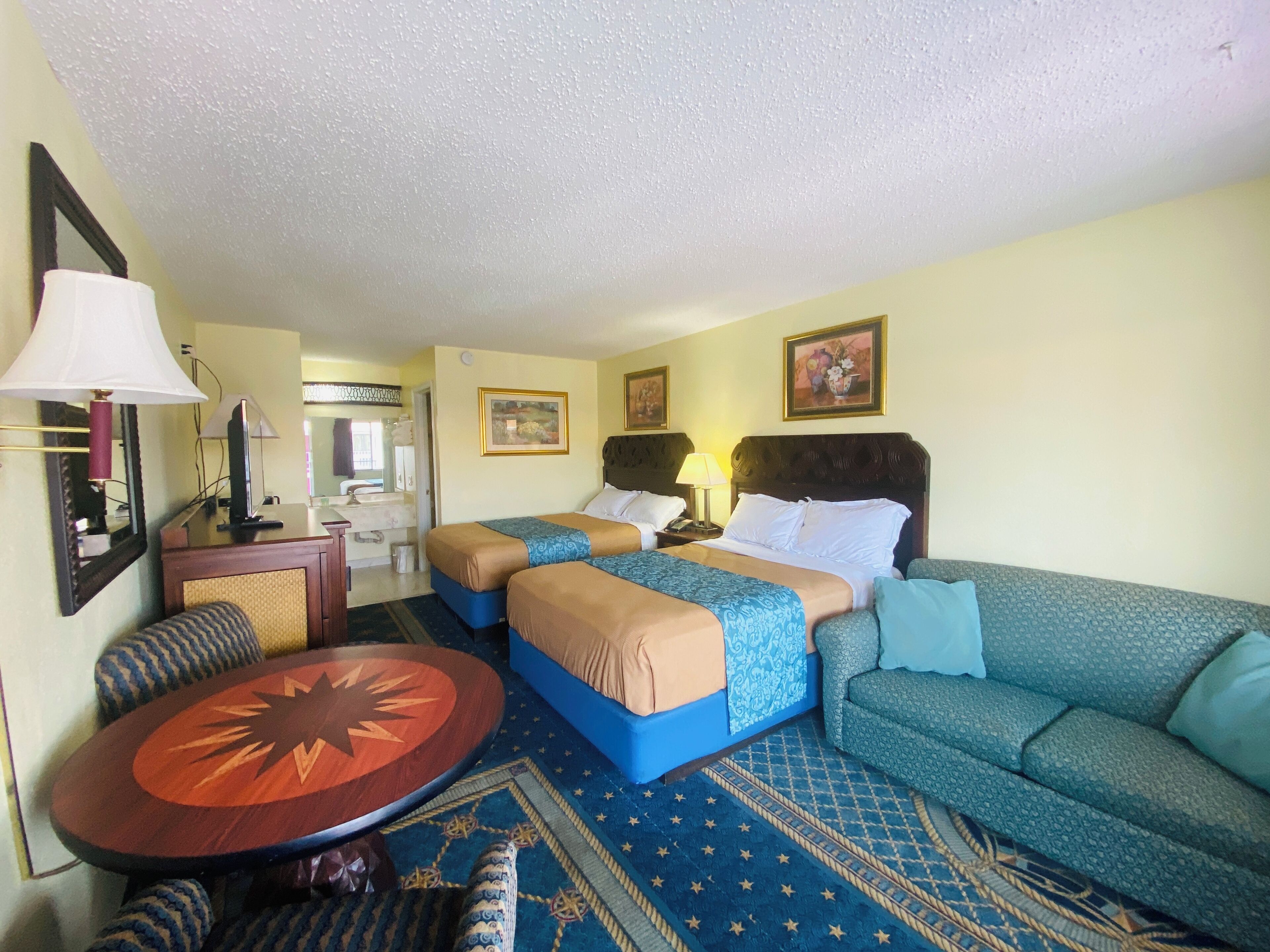 Habitación de hotel con dos camas, un sofá, una mesita y un espejo.