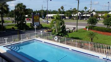 A swimming pool with a white fence, surrounded by greenery and palm trees.
