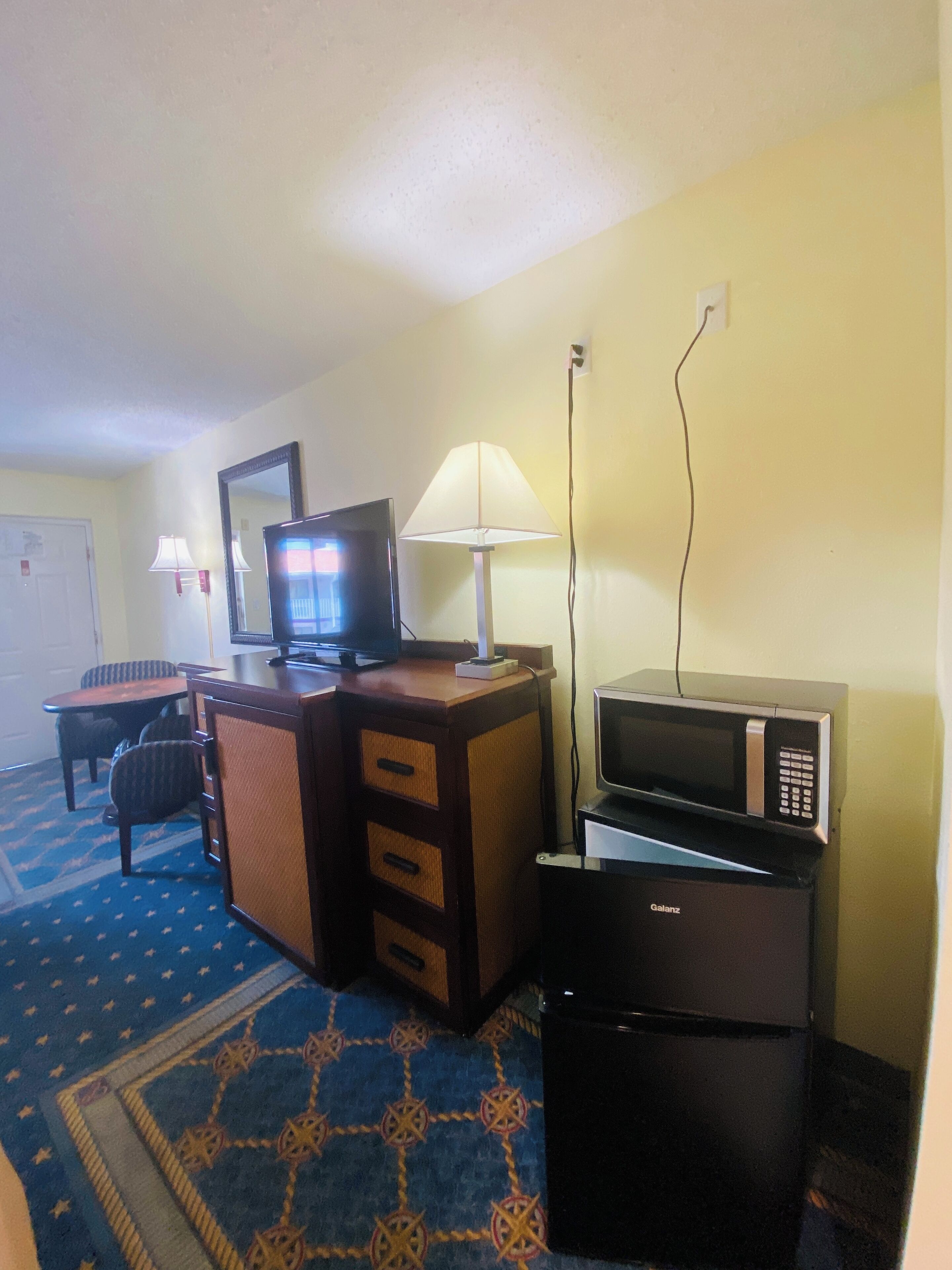 A hotel room with a desk, a television, a microwave, and a lamp.