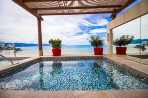 Una piscina con mosaicos, rodeada de macetas rojas y una pérgola.