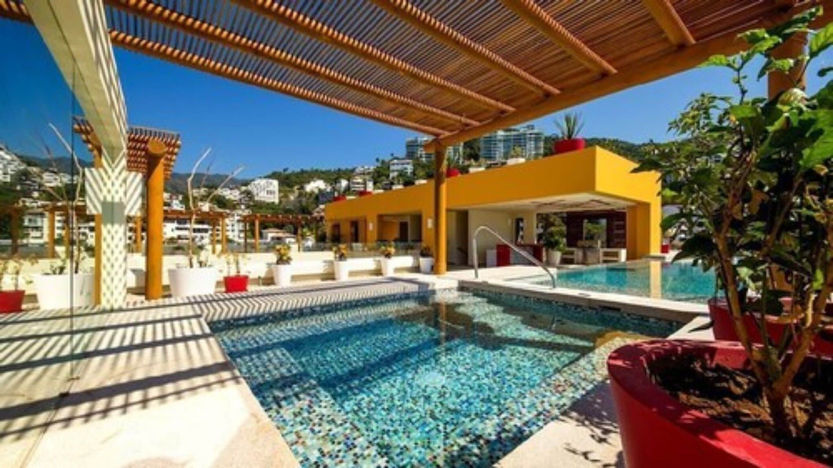 Area piscina con piscina cristallina azzurra, lettini prendisole e zona salotto coperta.
