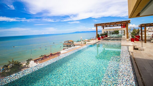 Una piscina con diseño de mosaicos, una pérgola de madera y vista al mar.
