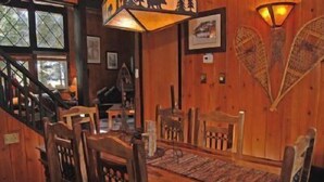 Un comedor de madera con una mesa y sillas, una escalera y apliques de luz en la pared.