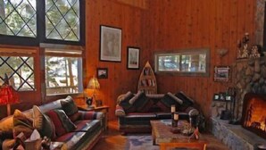 Interior acogedor de una cabaña con chimenea, paredes de madera y un ventanal grande.