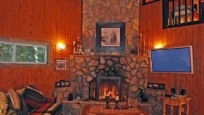 Una habitación acogedora con chimenea de piedra, paredes de madera, un sofá confortable y una televisión.