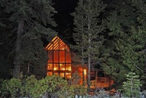 Mökki, jonka katto on kolmion muotoinen, ja jonka ympärillä on tiheää metsää.