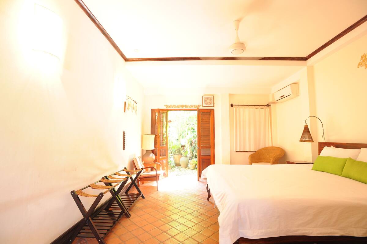 Une chambre d’hôtel avec un lit, une chaise, une lampe et une fenêtre.