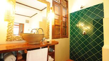 A bathroom with a large mirror, wooden vanity, and a green tiled shower area.