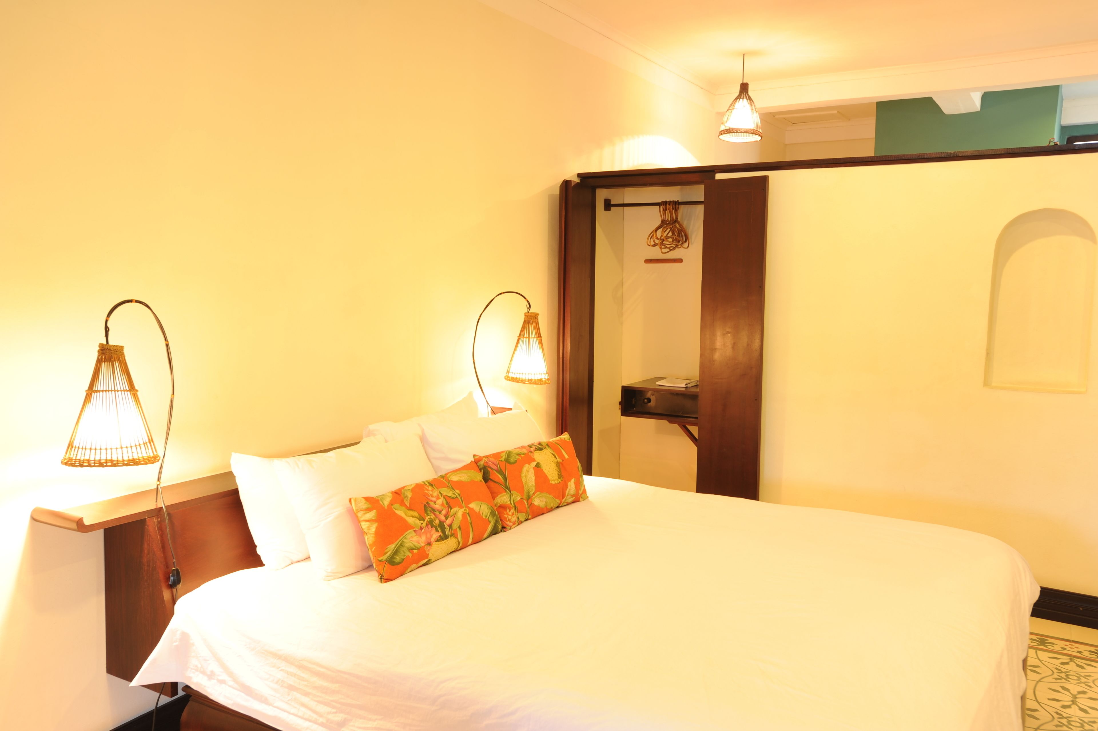 A hotel room with a bed, two bedside lamps, a nightstand, and a door leading to another room.