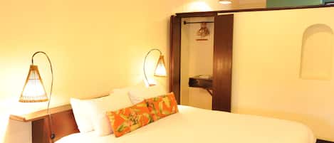 A hotel room with a bed, two bedside lamps, a nightstand, and a door leading to another room.