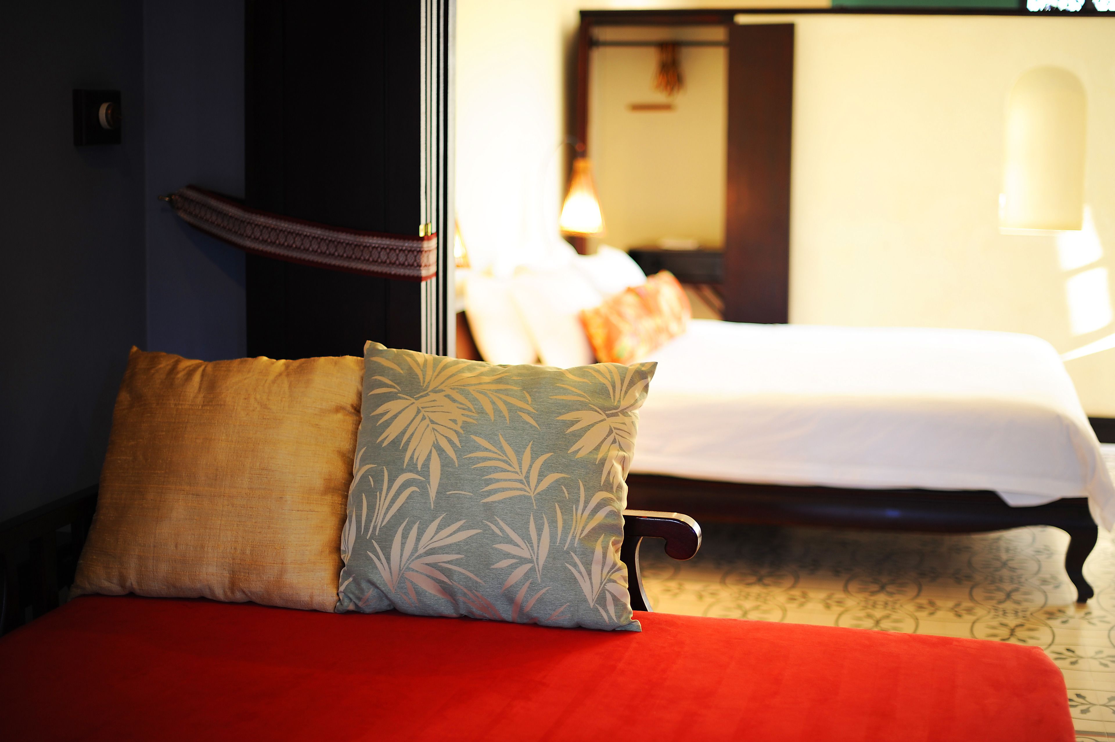 A hotel room with a bed, a red sofa, and a large mirror reflecting the room.